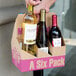 A hand holding a 6 pack cardboard wine bottle carrier with a bottle on a table.