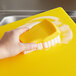 A hand cleaning a yellow cutting board with a yellow brush.