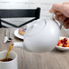 A hand pouring tea into a white Schonwald teapot.