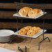 A Clipper Mill gray iron powder coated 2 tier square riser with bagels on plates.