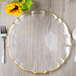 A Charge It by Jay clear glass charger plate with a gold rim on a table with a fork and knife.