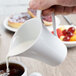 A person pouring milk from a Schonwald porcelain creamer into a cup of coffee.