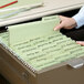 A person putting a Smead FasTab file into a file drawer filled with folders.