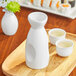 A white Acopa sake bottle and cups on a wooden tray.