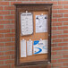 A wooden enclosed bulletin board with cork and papers on it.