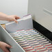 A hand holding a file folder opening a file cabinet with several Smead Legal Size File Folder boxes inside.