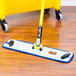 A blue Rubbermaid HYGEN wet mop pad attached to a yellow mop handle on a wood floor.