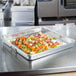 A Vollrath aluminum roasting pan with vegetables on a counter.