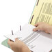 A person's hands using a Smead SafeSHIELD folder to hold paper with a pen
