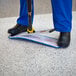 A person in blue pants and black boots using a Rubbermaid Pulse Spray Mop Kit on a blue mat.