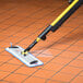 A Rubbermaid Pulse mop with a yellow handle cleaning a tile floor.