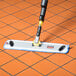 A Rubbermaid HYGEN Pulse mop with a yellow and black handle being used to clean a tile floor.