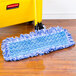 A blue Rubbermaid wet mop pad with hook and loop ends on a wooden floor.