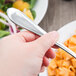A hand holding a Libbey stainless steel dinner fork over a plate of pasta and salad.