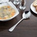 A bowl of soup next to a plate of bread and a Libbey stainless steel bouillon spoon.