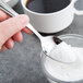 A person holding a Libbey Cortland stainless steel teaspoon filled with white sugar.