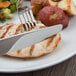 A Libbey stainless steel dinner knife and fork cutting meat on a plate of food.