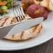 A Libbey stainless steel fluted hollow handle dinner knife and fork on a plate of food cutting meat.