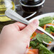A hand holding a Libbey stainless steel salad fork over a plate of salad.