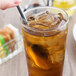 A hand holding a World Tableware stainless steel iced tea spoon in a glass of iced tea.
