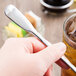 A hand holding a World Tableware stainless steel iced tea spoon over a glass of ice.