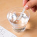 A hand holding a Purell Active Ingredient Concentration test strip over a glass of water.