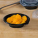 A bowl of oranges in a Fabri-Kal plastic container on a table.