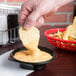 A person dipping a potato chip into a bowl of cheese sauce.