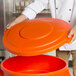 A chef places an orange Carlisle Bronco trash can lid on a container.
