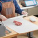 A person in a brown apron cutting Choice white butcher paper on a wood table over a white surface with a piece of meat.