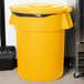 A yellow Carlisle Bronco trash can lid with a black handle.