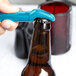 A person using a Franmara turquoise plastic bottle opener to open a brown bottle.