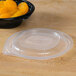 A Fabri-Kal plastic bowl with a vented lid holding oranges on a table.