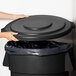 A person putting a Carlisle black round trash can lid on a black round trash can.