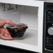 A hand using a Fabri-Kal SideKicks bowl to heat food in a microwave.