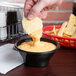 A person dipping a chip into a bowl of cheese sauce using a Fabri-Kal SideKicks bowl.