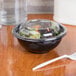 A Sabert clear plastic lid on a bowl of salad with a plastic fork.