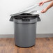 A person opening a Continental Huskee grey trash can with a grey lid to throw away a white plate.