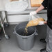 A man pouring grains into a Continental Huskee trash can in a school kitchen.