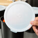A hand holding a white Cambro plastic lid.