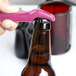 A hand using a pink Franmara Traveler's corkscrew and bottle opener to open a brown bottle.