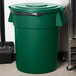 A green Carlisle Bronco trash can lid with a black handle.