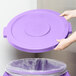 A person placing a purple Carlisle Bronco lid on a purple trash can