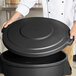 A person holding a Carlisle black round trash can lid.
