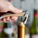 A hand using a Laguiole waiter's corkscrew with beechwood handle to open a bottle of wine.