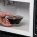 A hand holding a Fabri-Kal plastic container with food in a microwave.