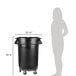 A woman standing next to a Rubbermaid black round trash can with lid and dolly.