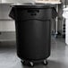A black Rubbermaid BRUTE 55 gallon garbage can with a lid on wheels.