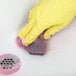 A hand in a yellow glove using a Scrubble steel wool soap pad to clean a sink.