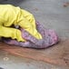 A person wearing yellow gloves using a Scrubble steel wool soap pad to clean wood.